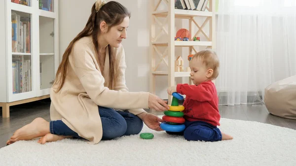 かわいいです赤ちゃん男の子組み立てカラフルなおもちゃの塔とともに彼の母親で床にリビングルーム — ストック写真