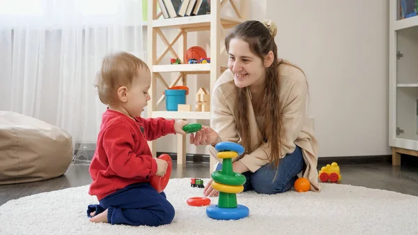笑着妈妈和她的小儿子在地毯上玩耍 还送给他五颜六色的玩具 — 图库照片