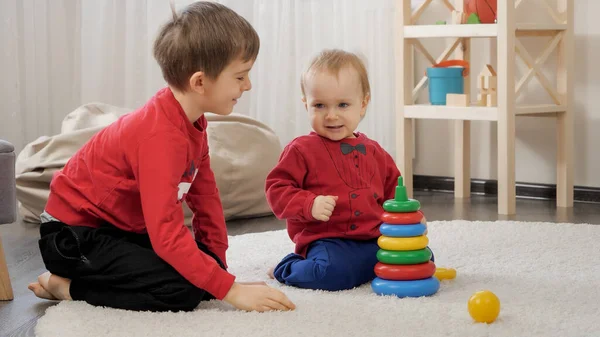 在客厅的地毯上和他的小弟弟一起玩玩具的大男孩笑着 — 图库照片