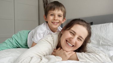 Mutlu neşeli çocuk, annesiyle yatakta uzanıyor ve ona sarılıyor. Mutlu aile kavramı, çocuklu ebeveynler, olumlu duygular ve evde rahatlama.