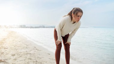 Kumlu deniz sahilinde koşan ve nefes almak için mola veren genç ve zinde bir kadının ağır çekimleri. Doğada sağlıklı yaşam tarzı, spor ve spor kavramı