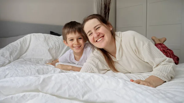 優しいベッドの上に寝そべっている笑顔の息子と幸せな陽気な母親 家族の幸福の概念 自宅でリラックス ベッドで楽しみを持っています 親と陽気な子供 — ストック写真