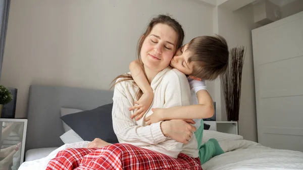 Młody Troskliwy Kochający Chłopiec Przytulający Swoją Zdenerwowaną Matkę Siedzącą Łóżku — Zdjęcie stockowe