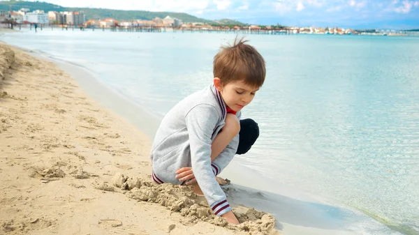 Young Boy Sits Sunny Beach Digging Hands Warm Sand Enjoys — Stock Photo, Image