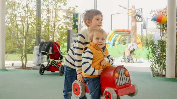 大男孩骑着他的小弟弟在孩子们的操场上骑春车 — 图库照片