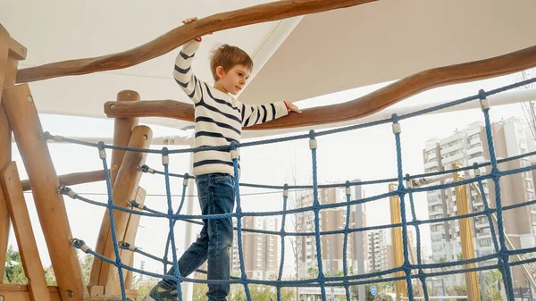 Mały Chłopiec Balansujący Drewnianym Moście Linowym Placu Zabaw Parku — Zdjęcie stockowe