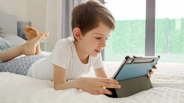 小男孩躺在床上 平板电脑正享受着他的银幕时光 使用小工具的儿童 教育和发展 — 图库照片