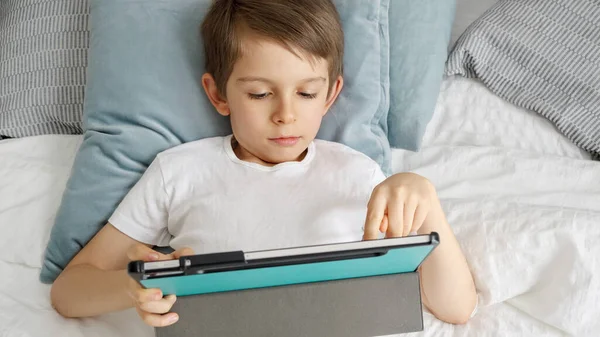 小さな男の子がベッドの上に横になり 日中タブレットPcで遊んでいます ガジェット 教育と開発を使用して子供 — ストック写真