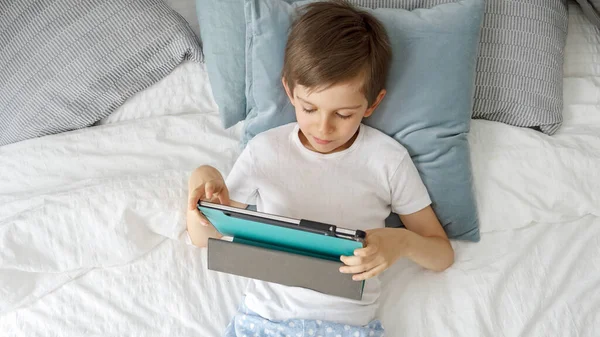 昼間寝そべっている間にタブレットを使っている少年 彼の視線はスクリーンに固定されている ガジェット 教育と開発を使用して子供 — ストック写真