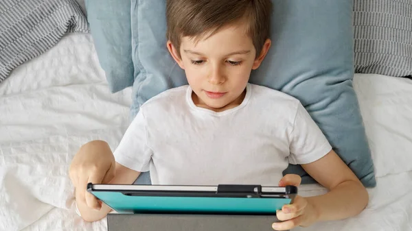 一个白天躺在床上用平板电脑的男孩 使用小工具的儿童 教育和发展 — 图库照片