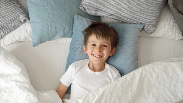 Szczęśliwy Chłopczyk Leżący Łóżku Otwierający Koc Uśmiechem Skierowanym Kamery — Zdjęcie stockowe