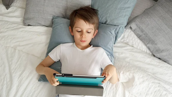 Radosny Chłopiec Jest Szczęśliwy Korzystając Tabletu Podczas Leżenia Łóżku Ciągu — Zdjęcie stockowe