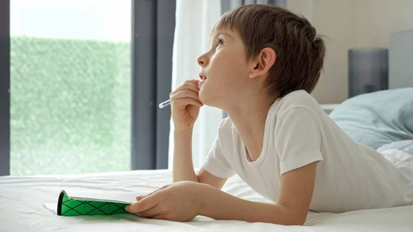 Mały Chłopiec Leżący Łóżku Odrabiający Lekcje Gryzący Ołówek Myśląc Pojęcie — Zdjęcie stockowe