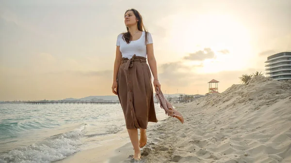 一个戴着丝巾的年轻女子在日落时分走在沙滩上 旅行和假日的概念 — 图库照片
