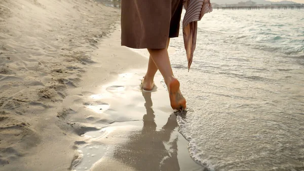 夕焼けの砂浜で濡れた砂と海の波を歩く裸足の女性の閉鎖 — ストック写真