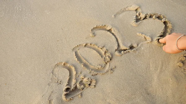 指で2023年を海の砂の上に書くために女性の手の閉鎖 — ストック写真