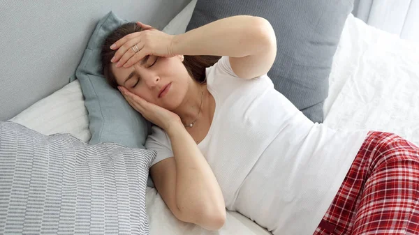 若い病気の女性が高い温度がベッドに横たわっていると頭痛に苦しんでいる間額に手を保持 — ストック写真