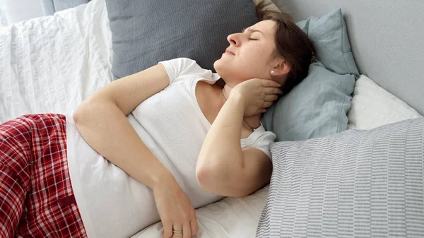 穿着睡衣的年轻女人睡在不舒服的床上和枕头上 感到脖子疼痛 — 图库照片