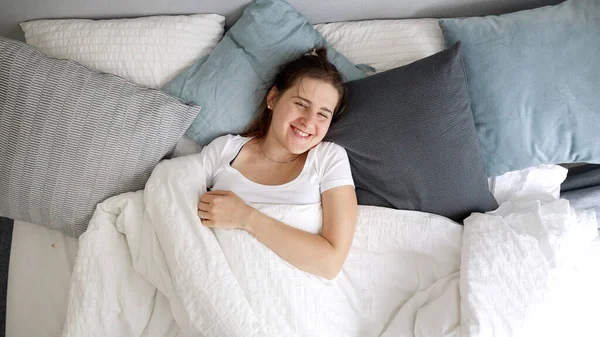 快乐的女人一边躺在床上一边扔毯子 一边对着镜头笑 家庭快乐 周末放松 早上快乐的概念 — 图库照片
