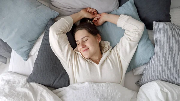 リラックスした若い女性は柔らかい枕の上に横になり 午前中にベッドでストレッチ 快適さ リラクゼーション 健康的な睡眠と新しい一日の良いスタートの概念 — ストック写真