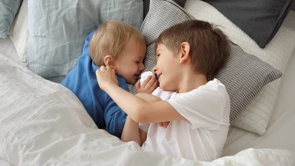 Dwóch Słodkich Chłopców Leżących Łóżku Miękkich Poduszkach Uśmiechających Się Siebie — Zdjęcie stockowe