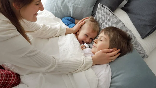 2人の息子を覆う若い思いやりのある母親は毛布でベッドに横たわってそれらを愛撫 家族の幸福の概念 自宅でリラックス ベッドで楽しみを持っています 親と陽気な子供 — ストック写真