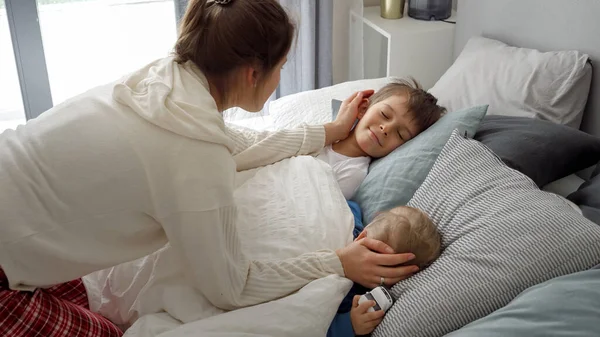 담요를 웃으면서 자녀들 침대에서 모습을 바라보는 스러운 어머니의 집에서 휴식을 — 스톡 사진