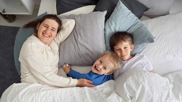 Счастливая Жизнерадостная Мать Двумя Сыновьями Лежащими Утром Постели Улыбающимися Камеру — стоковое фото