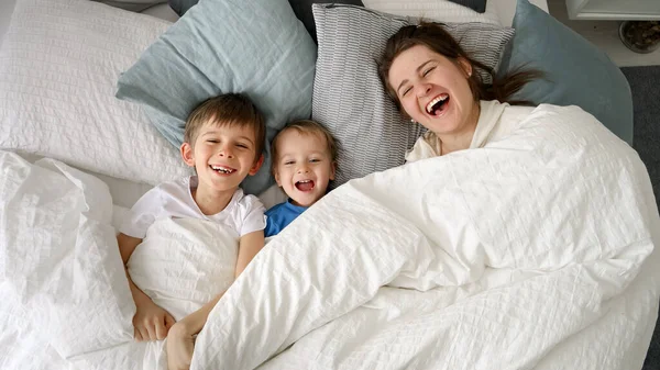 Feliz Família Rindo Com Dois Filhos Escondidos Debaixo Cobertor Cama — Fotografia de Stock