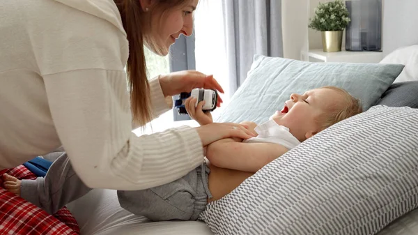 Młoda Opiekuńcza Matka Próbuje Ubrać Syna Leżącego Łóżku Krzyczącego — Zdjęcie stockowe