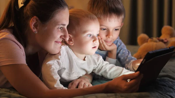 Pijamalı Iki Gülümseyen Kardeş Uyumadan Önce Annemle Tablet Bilgisayarda Oynuyorlar — Stok fotoğraf