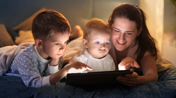 엄마는 아이들 침대에 누워서 태블릿 컴퓨터로 비디오 게임을 합니다 보내는 — 스톡 사진