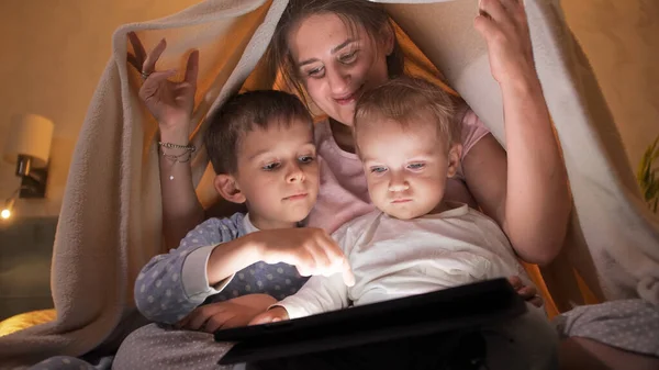 ベッドで遊んだり タブレットコンピュータでゲームをしたりして パジャマ姿の2人の息子と一緒に幸せな笑顔の母親 一緒に時間を過ごす家族 子育て 幸せな子供時代とエンターテイメント — ストック写真