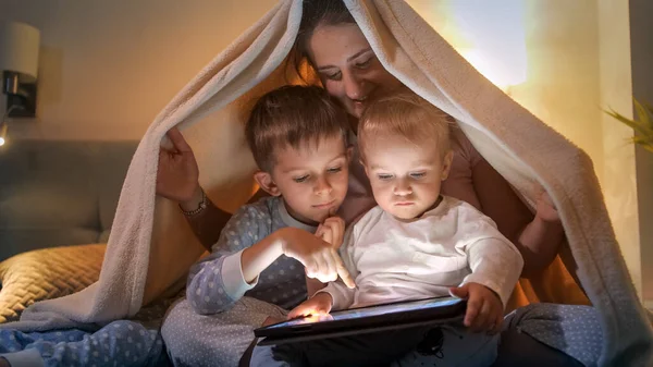 夜間に毛布の下に隠れ タブレットコンピュータを使用して笑顔の家族 一緒に時間を過ごす家族 子育て 幸せな子供時代とエンターテイメント — ストック写真