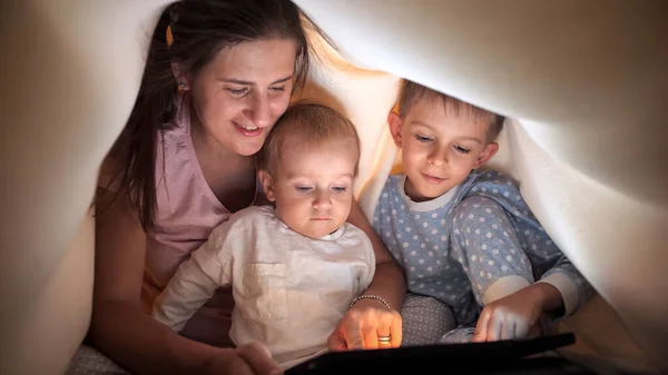 两个可爱的男孩 妈妈穿着睡衣 在平板电脑上玩耍 妈妈躺在床上 有时间在一起的家庭 养育子女 快乐的童年和娱乐 — 图库照片