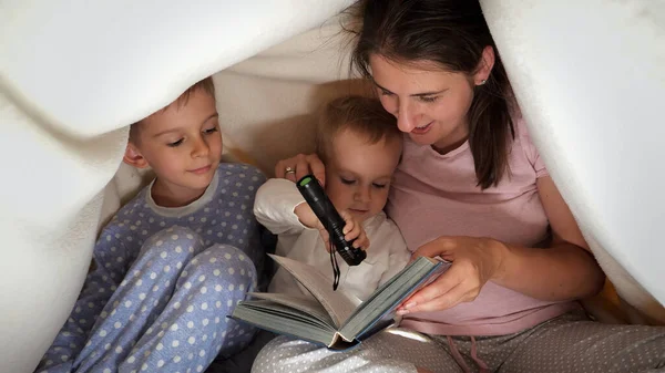 Два Маленьких Мальчика Сидят Мамой Кровати Одеялом Читают Книгу Фонариком — стоковое фото