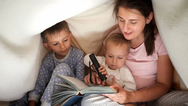 两个穿着睡衣的男孩晚上躲在毯子下听妈妈讲童话 有时间在一起的家庭 养育子女 快乐的童年和娱乐 — 图库照片