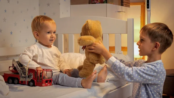 两个男孩晚上在床上玩泰迪熊和玩具车 有时间在一起的家庭 养育子女 快乐的童年和娱乐 — 图库照片