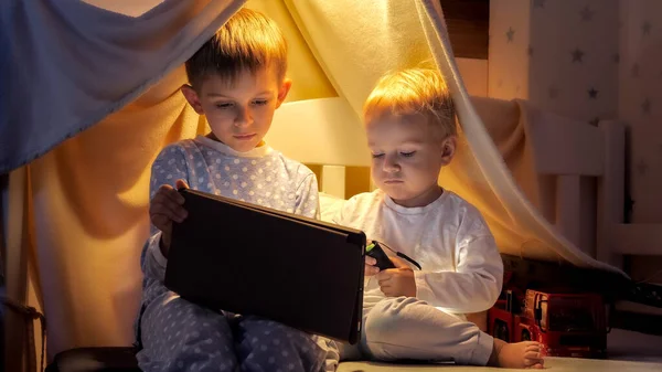 大哥哥的小男孩晚上睡觉前用平板电脑和在床上看视频 — 图库照片