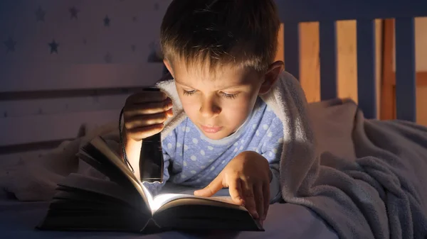 穿着睡衣的小男孩晚上醒来 用手电筒看书 儿童教育 — 图库照片
