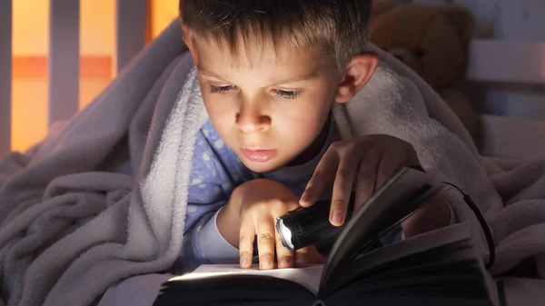 在床上抱着手电筒看书的男孩的衣服 儿童教育 — 图库照片