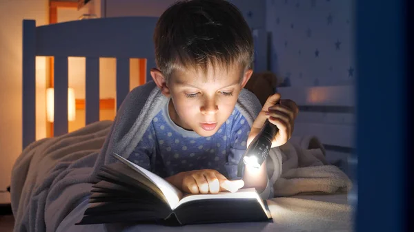 穿着睡衣的可爱男孩拿着手电筒看书的画像 儿童教育 — 图库照片
