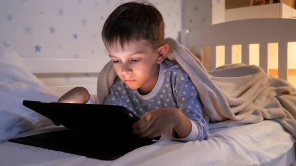 小男孩在睡觉前躺在床上 在平板电脑上浏览视频 — 图库照片