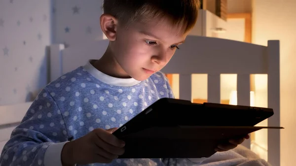 一个快乐微笑的男孩晚上坐在卧室里 在平板电脑上浏览互联网的画像 儿童教育 儿童使用小玩艺儿保密 — 图库照片