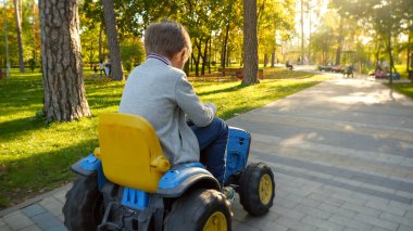 Küçük çocuk sonbahar parkında elektrikli oyuncak traktörü kullanırken eğleniyor. Çocuklar parkta oynar, çiftçilik yapar, taşıma araçları kullanır..