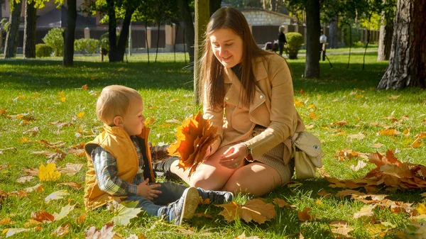 小男孩和妈妈坐在公园里 捡起秋天的黄叶 家庭户外 快乐的养育和童年 秋天的风景 — 图库照片
