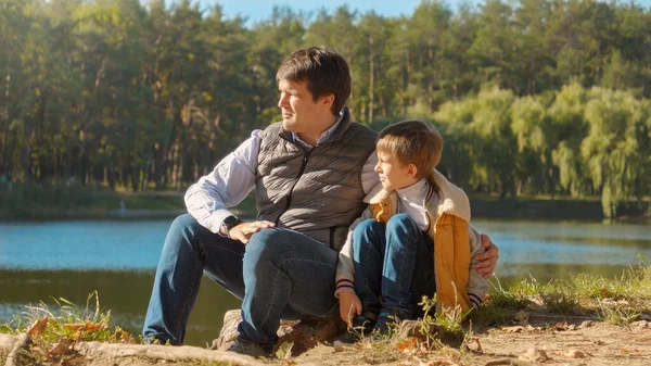 年轻有爱心的父亲坐在森林湖边和他的儿子说话 户外家庭 快乐的养育和童年 秋天的风景 孩子和父母在外面放松 — 图库照片