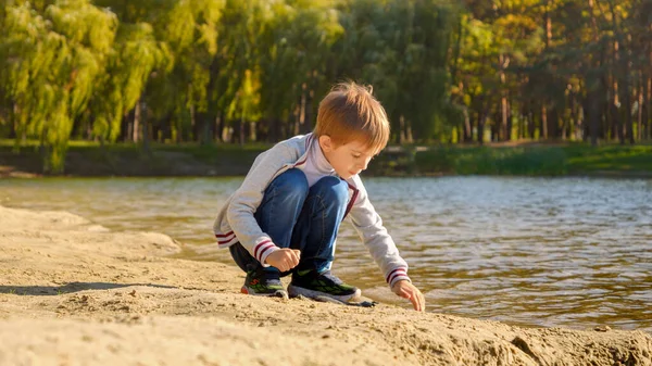 少年は川のビーチでぬれた砂で遊んでいる 屋外で遊ぶ子供 ビーチで遊ぶ子供 シティパークの湖 — ストック写真