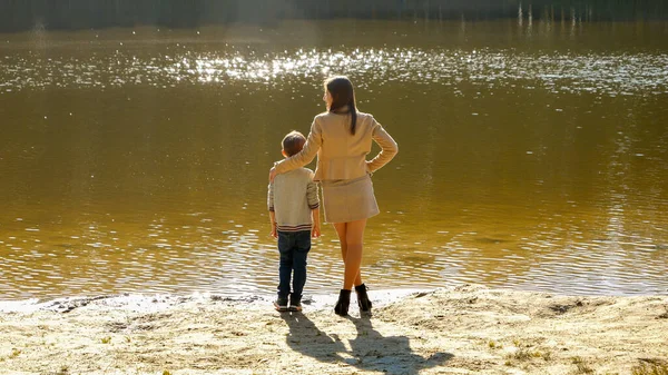 夕阳西下 妈妈站在河岸上的快乐男孩 户外家庭 快乐的养育和童年 秋天的风景 孩子和父母在外面放松 — 图库照片