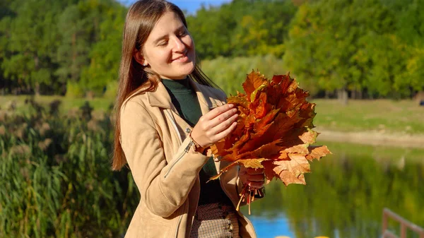 美丽的微笑的女人一边看着秋天的叶子 一边在公园的湖面上放松 美丽的大自然 陷在城市里 快乐的女人 — 图库照片